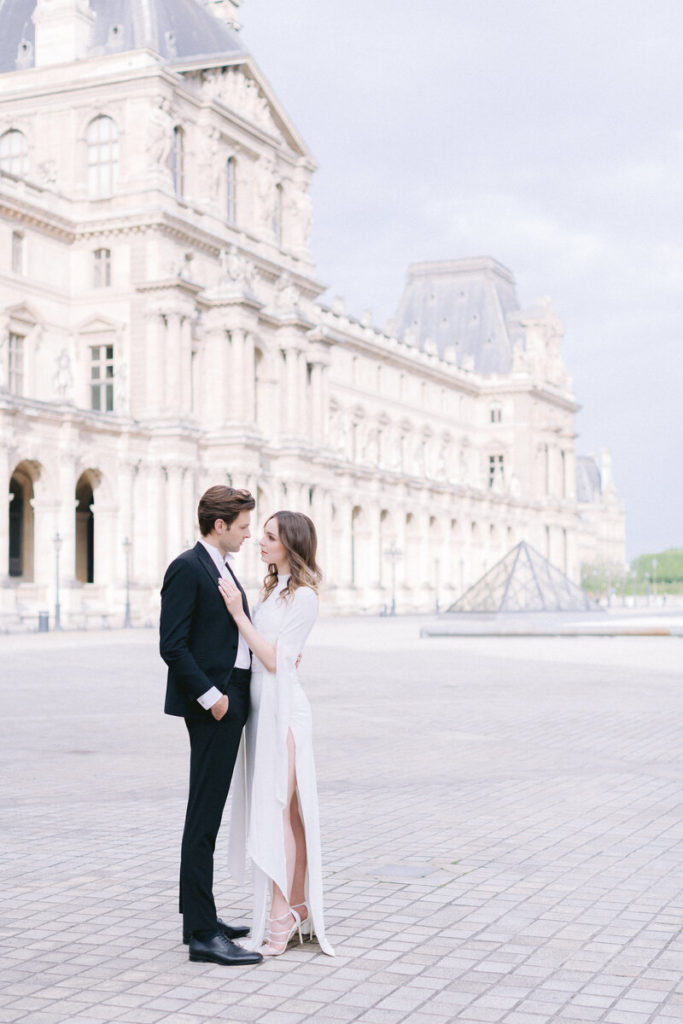Un couple se tenant debout cote à cote sur la place du Louvre à Paris lors d'un mariage intime