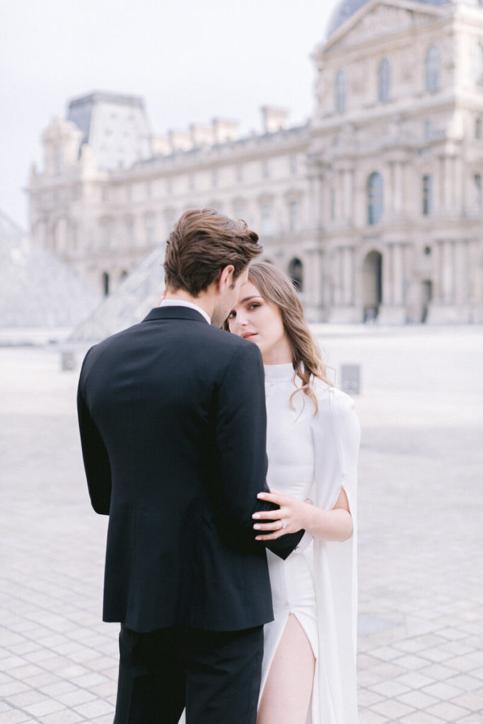 Un couple se tenant debout cote à cote sur la place du Louvre à Paris lors d'un mariage intime