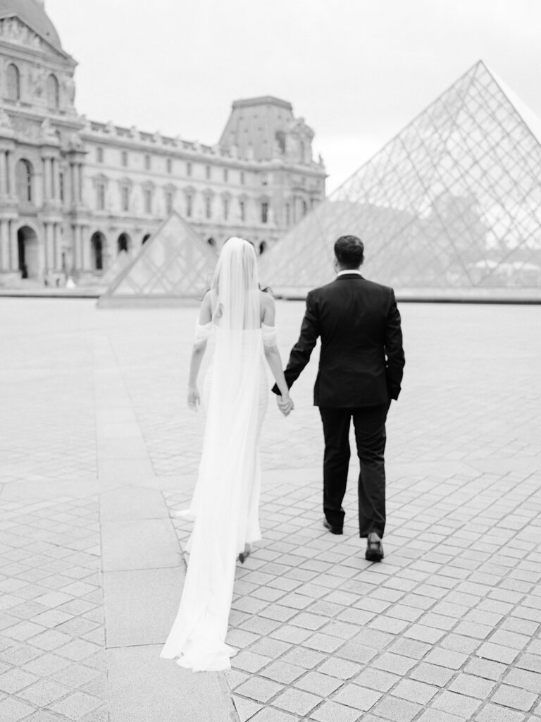 Bride and groom walking towards the Louvre Pyramid